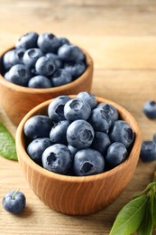 Photo of Bowls of fresh tasty blueberries on wooden table, closeup