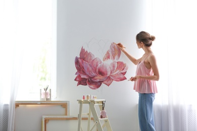 Photo of Decorator painting flower on white wall in room. Interior design