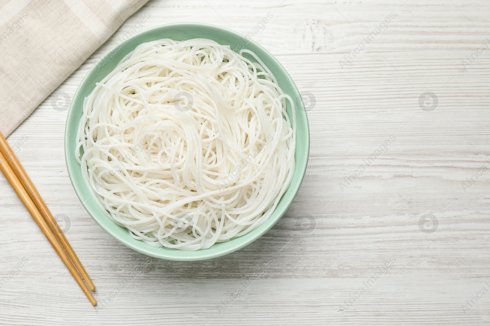 Photo of Bowl with cooked rice noodles and chopsticks on white wooden table, flat lay. Space for text