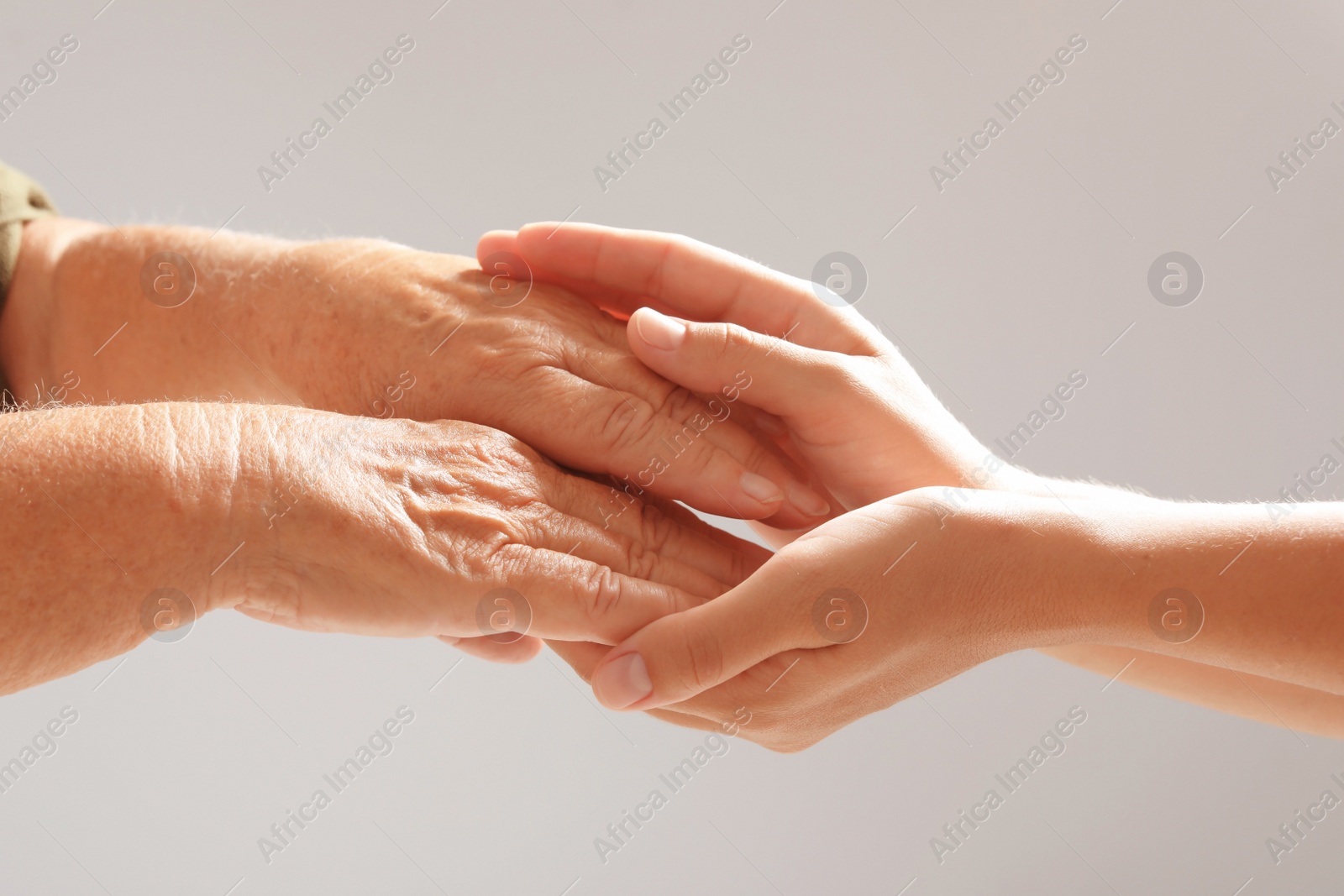 Photo of Helping hands on grey background, closeup. Elderly care concept