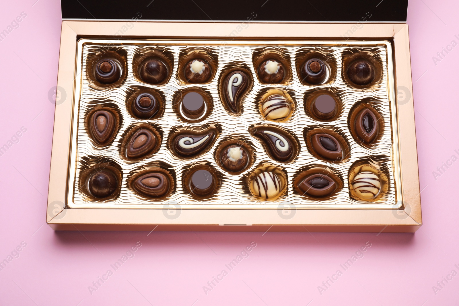 Photo of Box of delicious chocolate candies on pink background, closeup