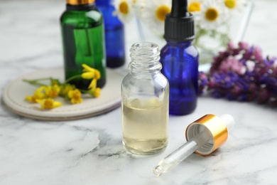 Bottles of different essential oils and wildflowers on marble table, space for text