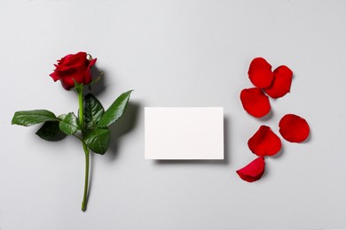 Photo of Blank card, beautiful red rose and petals on light background, flat lay. Space for text