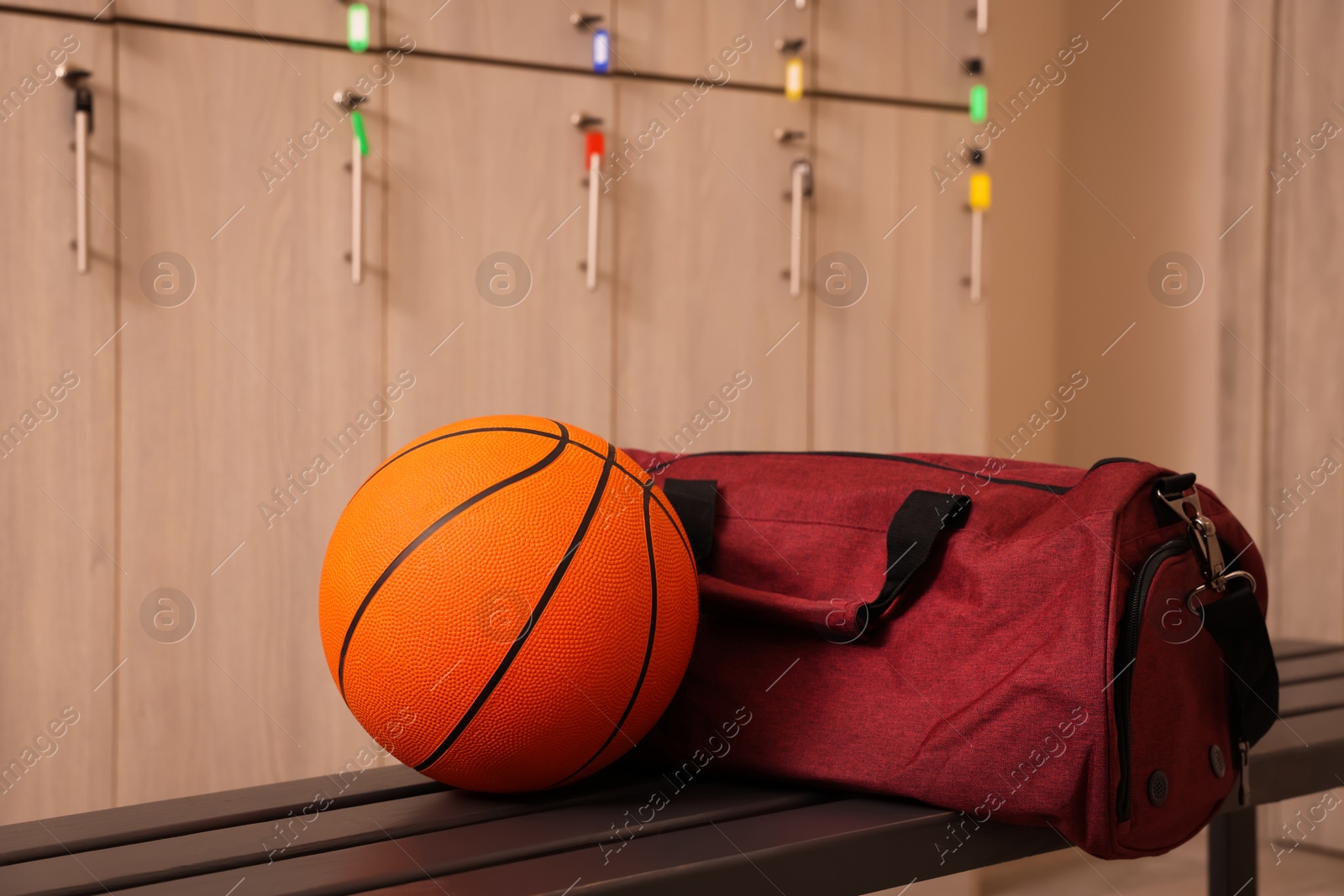 Photo of Sports bag and basketball ball on wooden bench in locker room