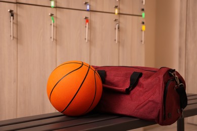 Photo of Sports bag and basketball ball on wooden bench in locker room