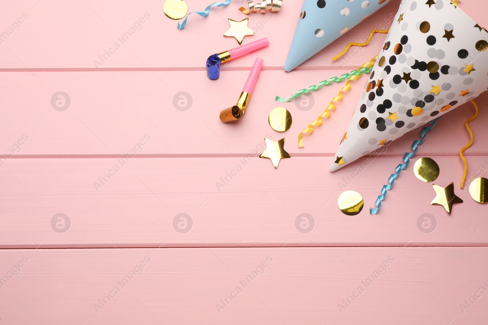 Photo of Flat lay composition with party hats, blowers and confetti on light pink wooden background. Space for text