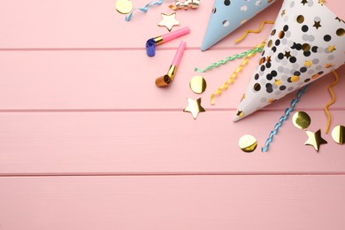 Flat lay composition with party hats, blowers and confetti on light pink wooden background. Space for text