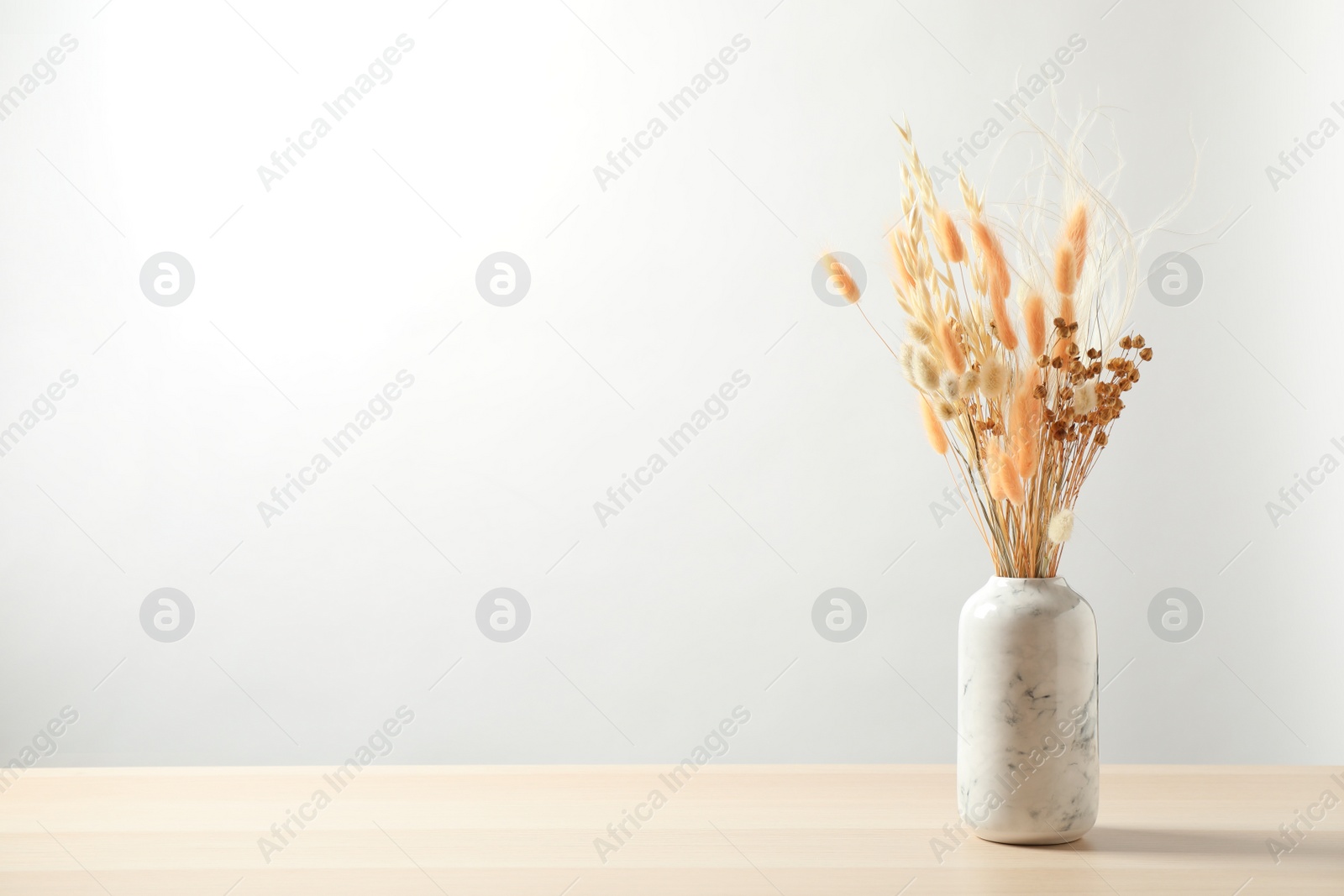 Photo of Dried flowers in vase on table against light background. Space for text