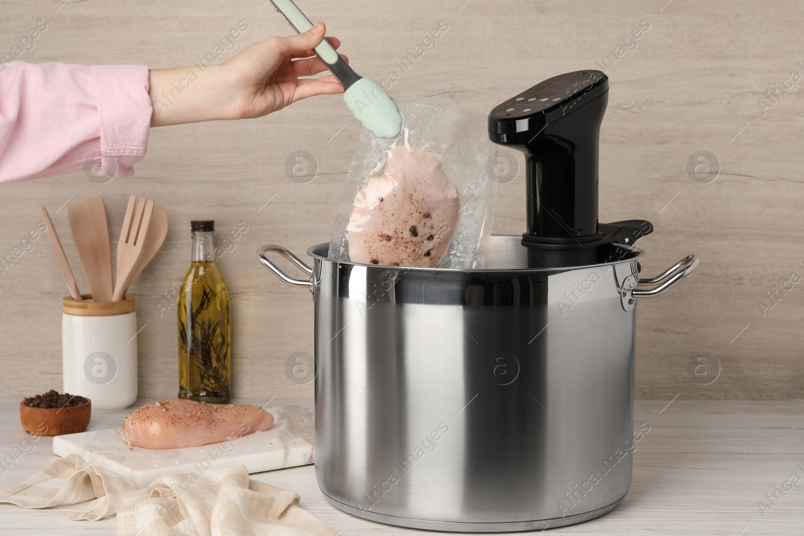 Photo of Woman putting vacuum packed meat into pot with sous vide cooker at table, closeup. Thermal immersion circulator