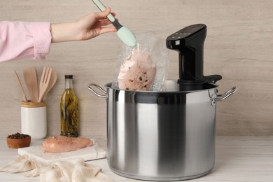 Photo of Woman putting vacuum packed meat into pot with sous vide cooker at table, closeup. Thermal immersion circulator