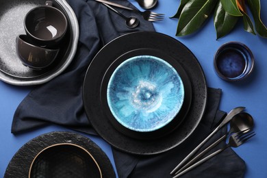 Photo of Stylish table setting. Dishware, cutlery and floral decor on blue background, flat lay