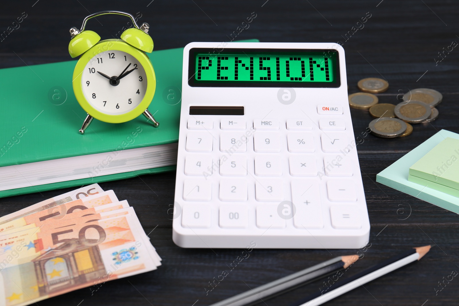 Image of Calculator with word Pension, money, alarm clock and stationery on dark wooden table, closeup