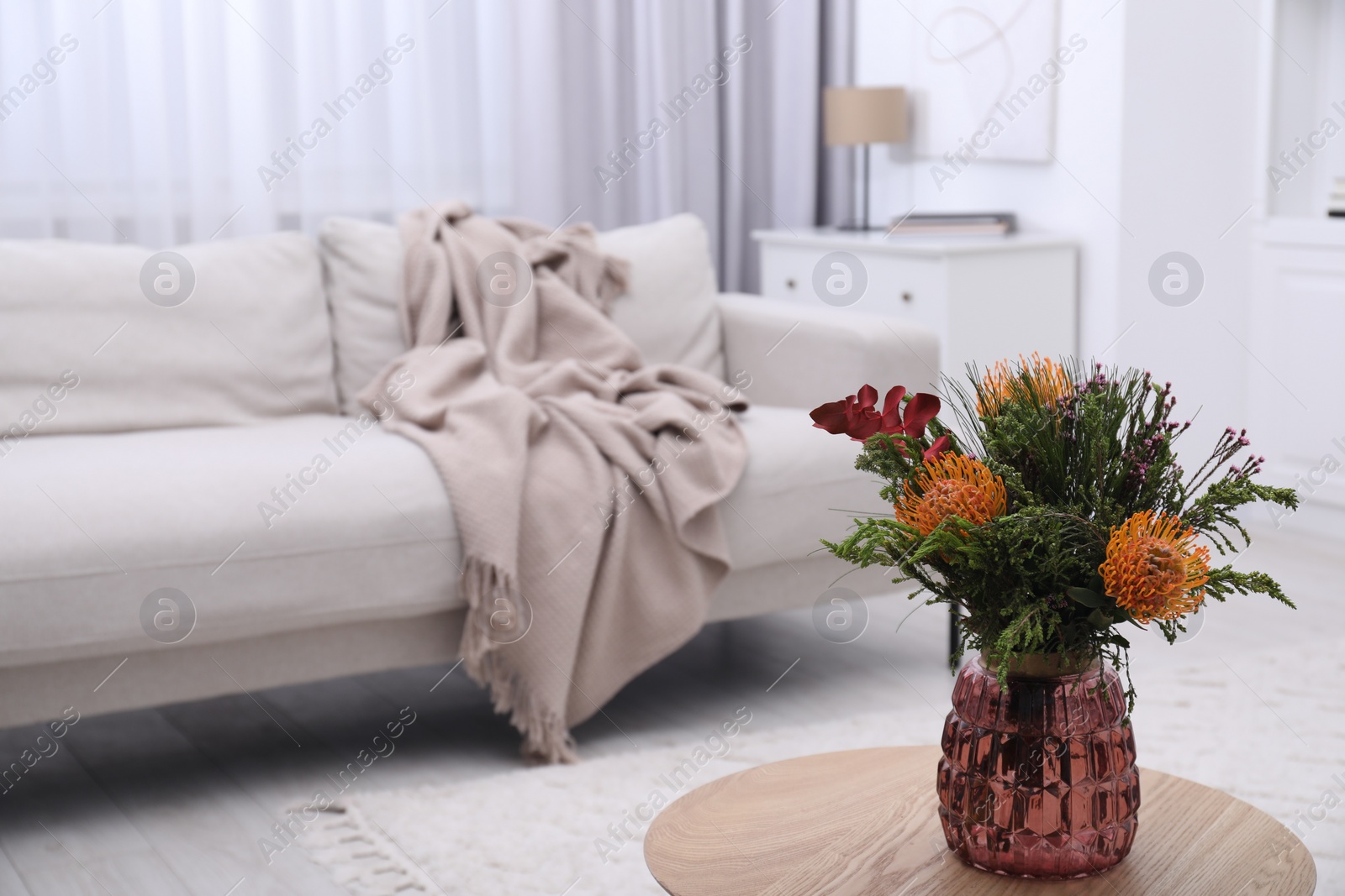 Photo of Vase with bouquet of beautiful leucospermum flowers on wooden table in living room