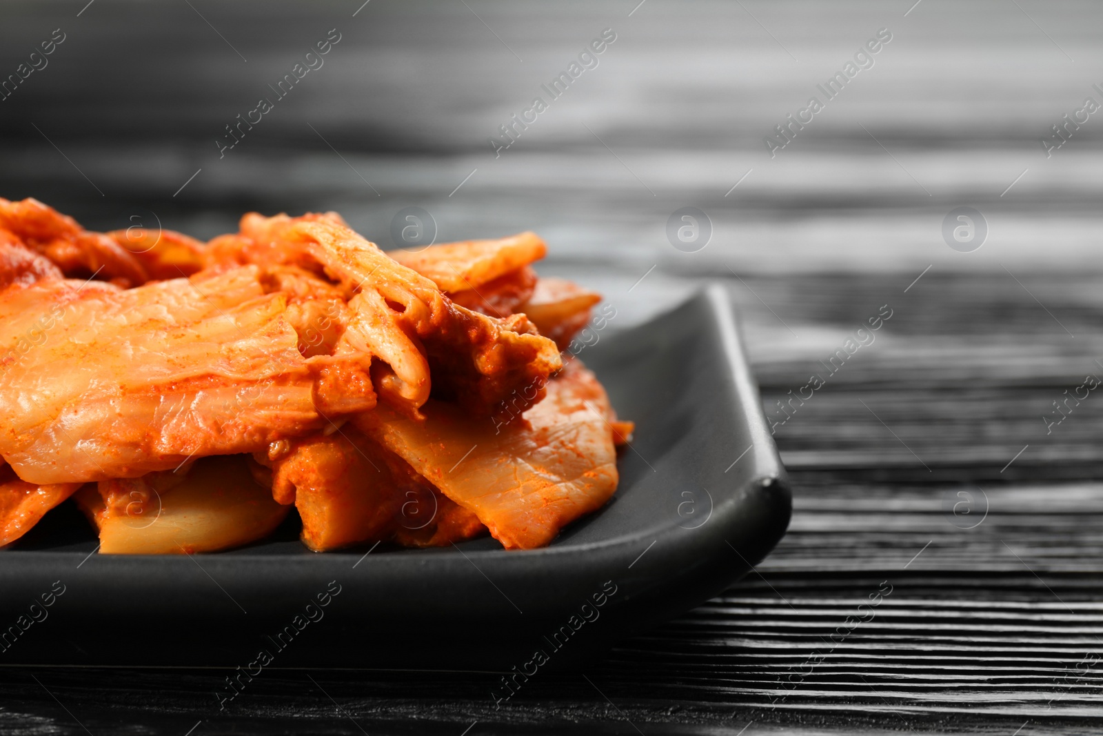 Photo of Delicious kimchi with Chinese cabbage on black wooden table, closeup