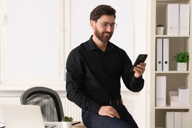 Photo of Smiling man in shirt using smartphone in office