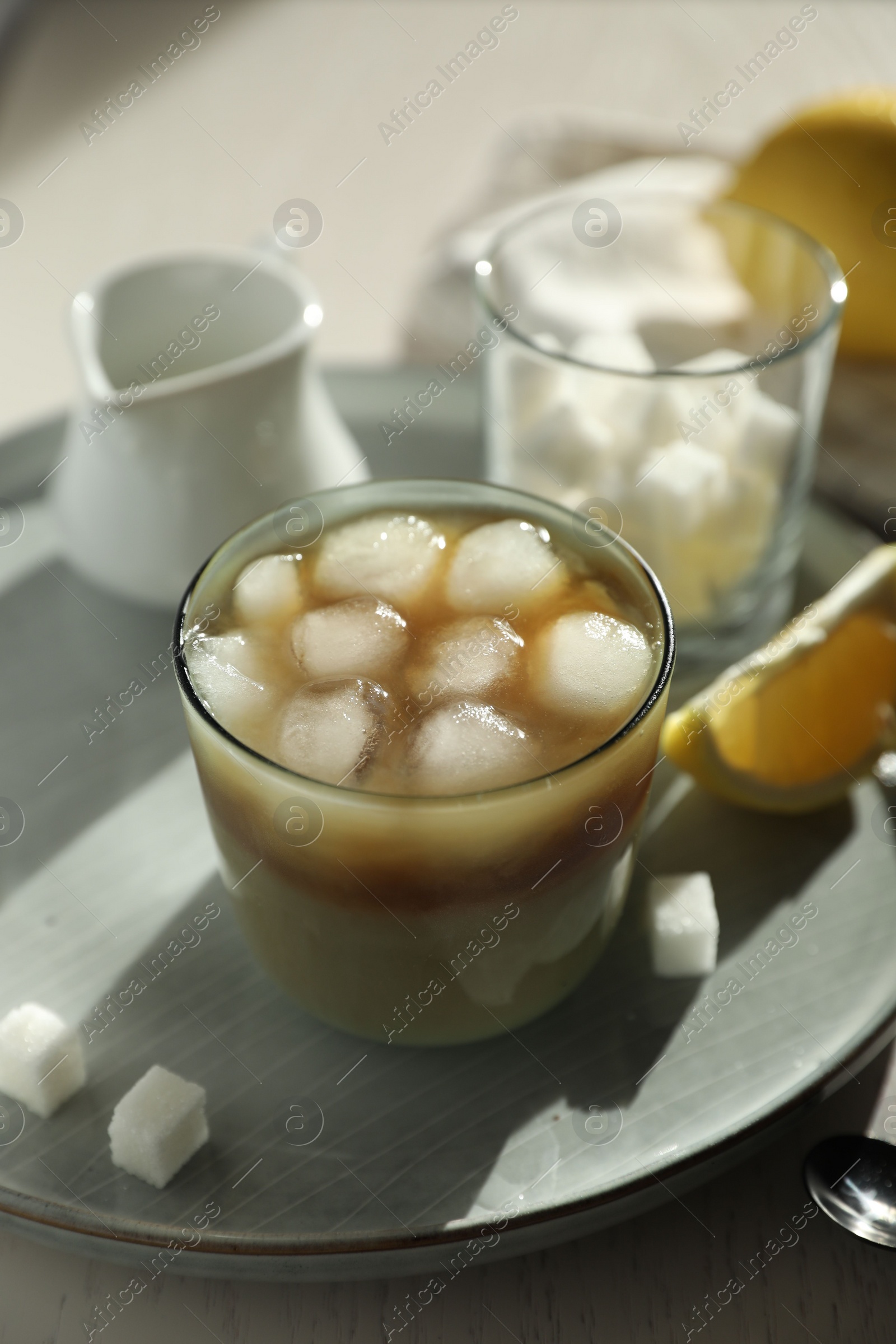 Photo of Refreshing iced coffee with milk in glass, sugar cubes and spoon on table, closeup