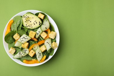 Photo of Bowl of tasty salad with tofu and vegetables on green background, top view. Space for text