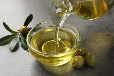 Photo of Pouring olive oil into glass bowl on grey table, closeup