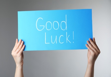 Woman holding blue card with words GOOD LUCK on light grey background, closeup