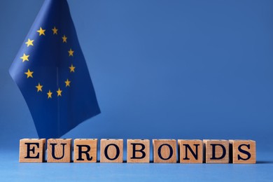 Photo of Word Eurobonds made of wooden cubes with letters and European Union flag on blue background