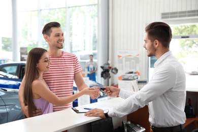 Salesman giving car key to happy couple in salon