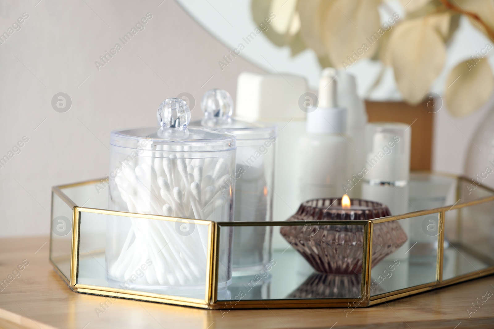 Photo of Containers with cotton swabs, pads and burning candle near cosmetic products on wooden table