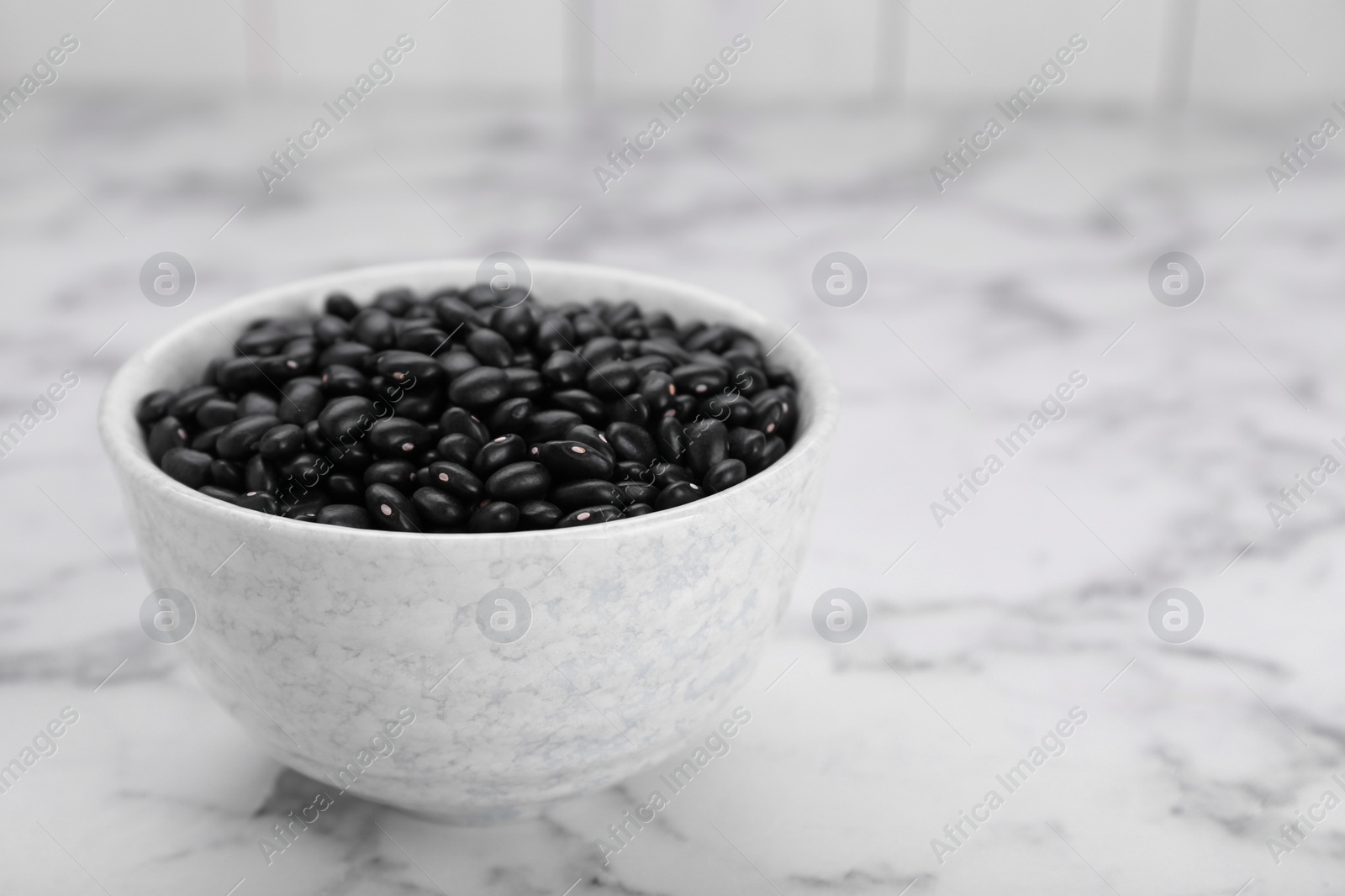Photo of Bowl of raw black beans on white marble table. Space for text