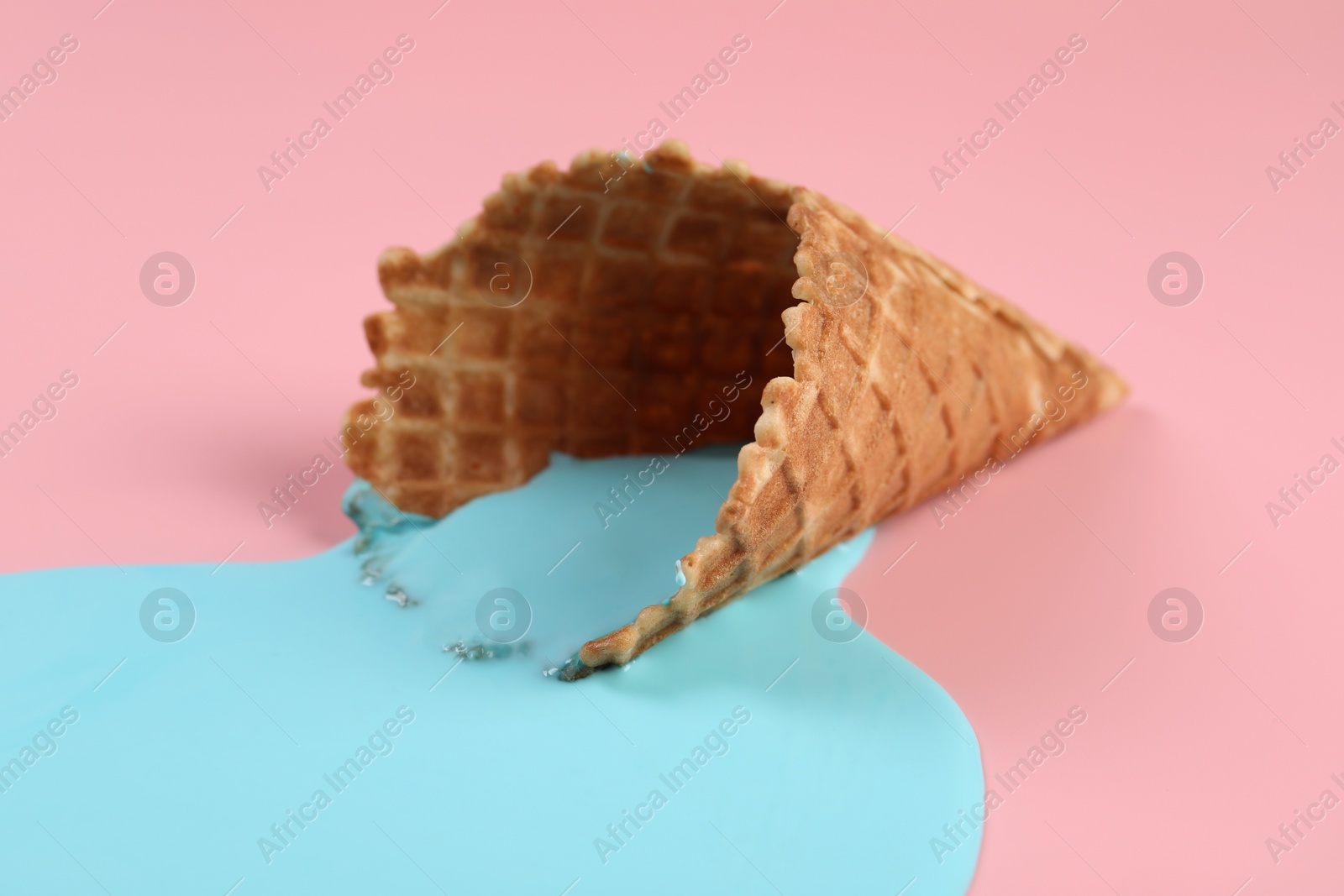 Photo of Melted ice cream and wafer cone on pink background, closeup