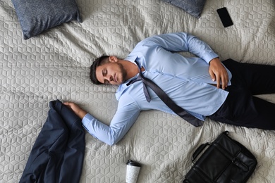 Exhausted businessman in office wear sleeping on bed at home after work, top view