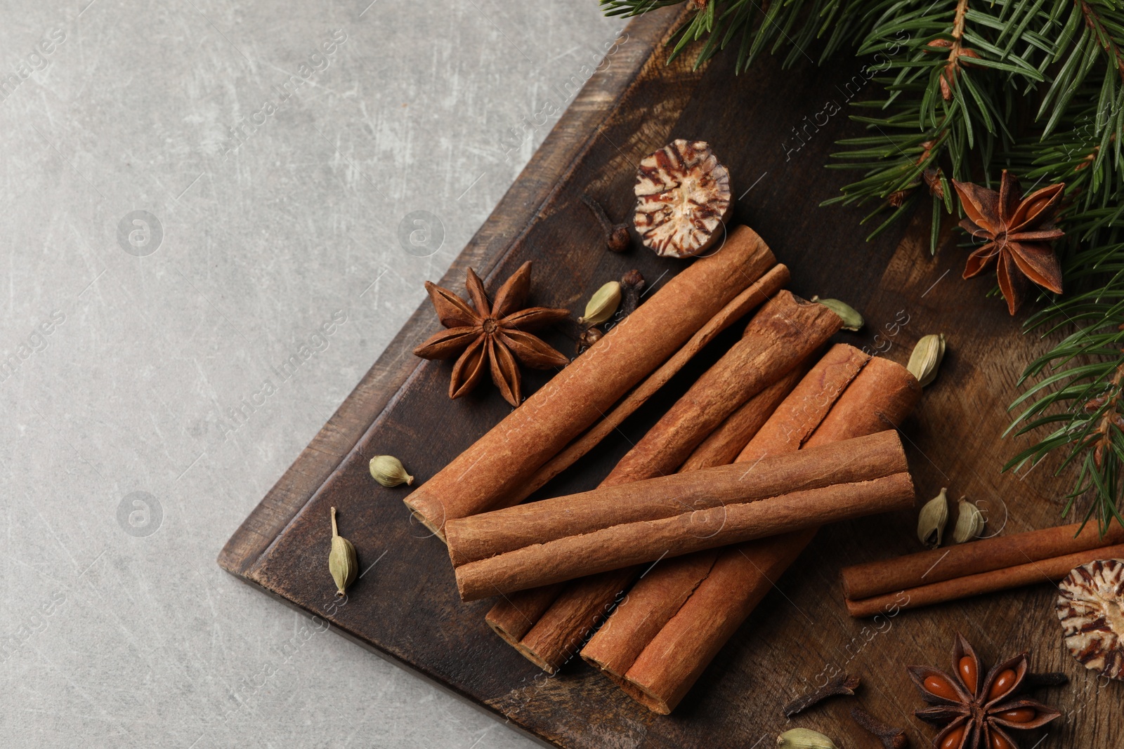 Photo of Board with different aromatic spices and fir branches on light table, top view. Space for text