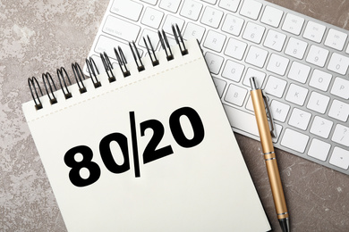 Image of Pareto principle concept. Notebook with 80/20 rule representation, pen and keyboard on grey background, flat lay