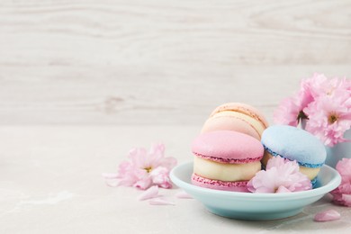 Delicious colorful macarons and pink flowers on light grey table, space for text