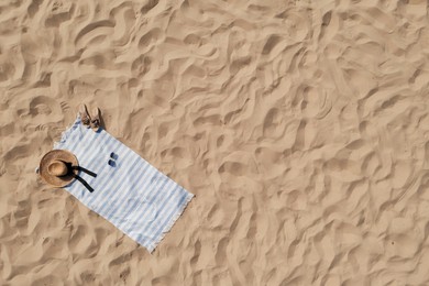 Towel with beach accessories on sand, top view. Space for text