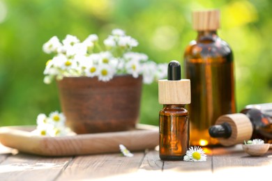 Photo of Bottles of chamomile essential oil and flowers on wooden table, space for text