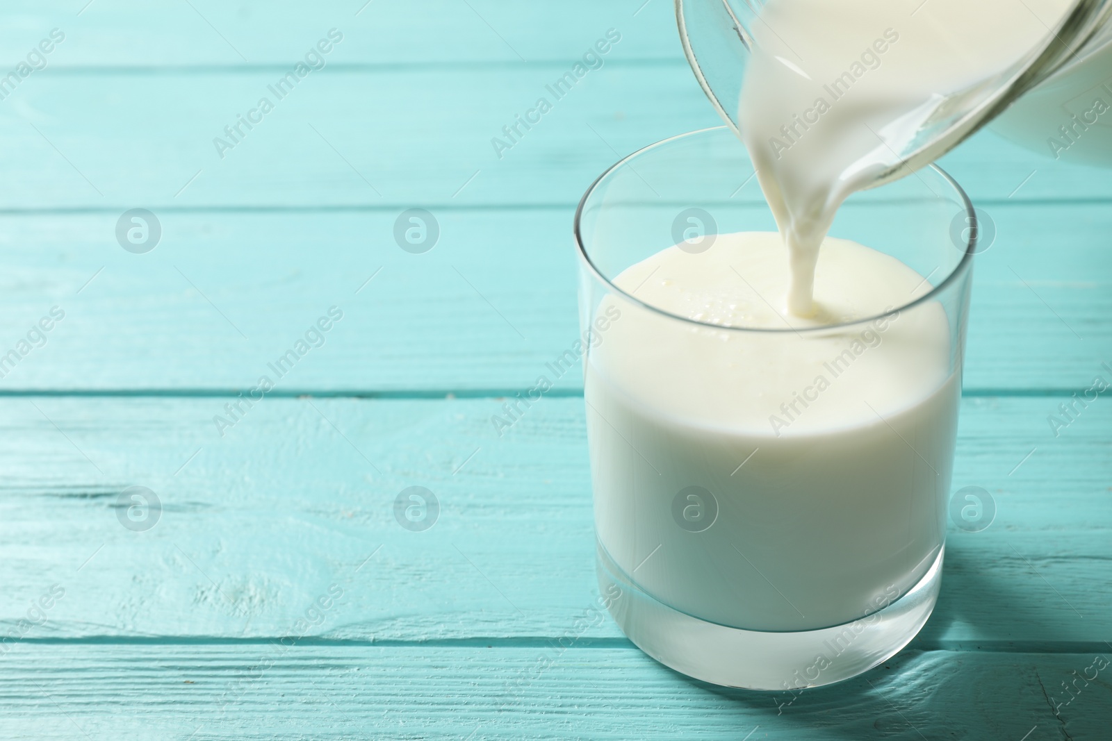 Photo of Pouring milk into glass on light blue wooden table. Space for text