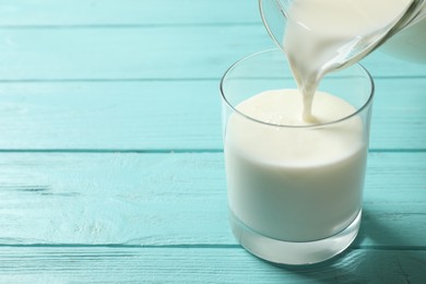 Photo of Pouring milk into glass on light blue wooden table. Space for text