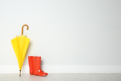 Photo of Colorful umbrella and rubber boots on floor against white wall. Space for text