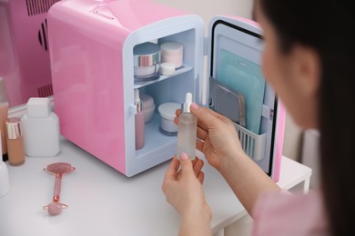 Woman taking cosmetic product out of mini refrigerator indoors, closeup