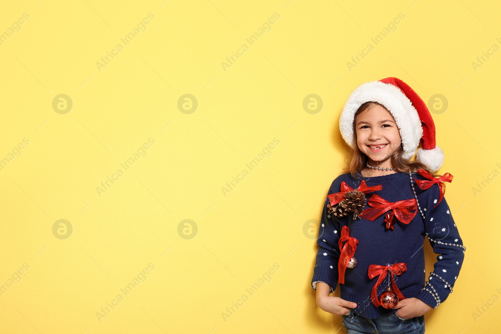 Photo of Cute little girl in handmade Christmas sweater on color background. Space for text