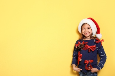 Cute little girl in handmade Christmas sweater on color background. Space for text