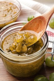 Photo of Jar, spoon with delicious gooseberry jam and fresh berries on wooden table, closeup
