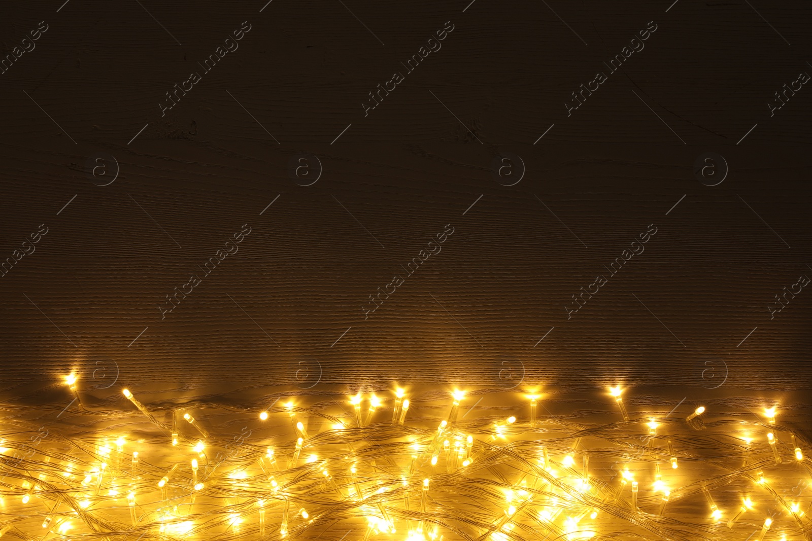 Photo of Beautiful glowing Christmas lights on wooden table, top view. Space for text