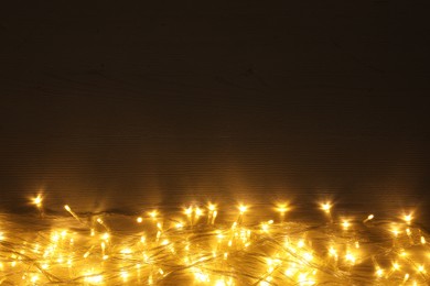 Beautiful glowing Christmas lights on wooden table, top view. Space for text