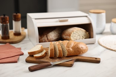 Photo of Wooden bread basket with freshly baked loaves and knife on white marble table in kitchen