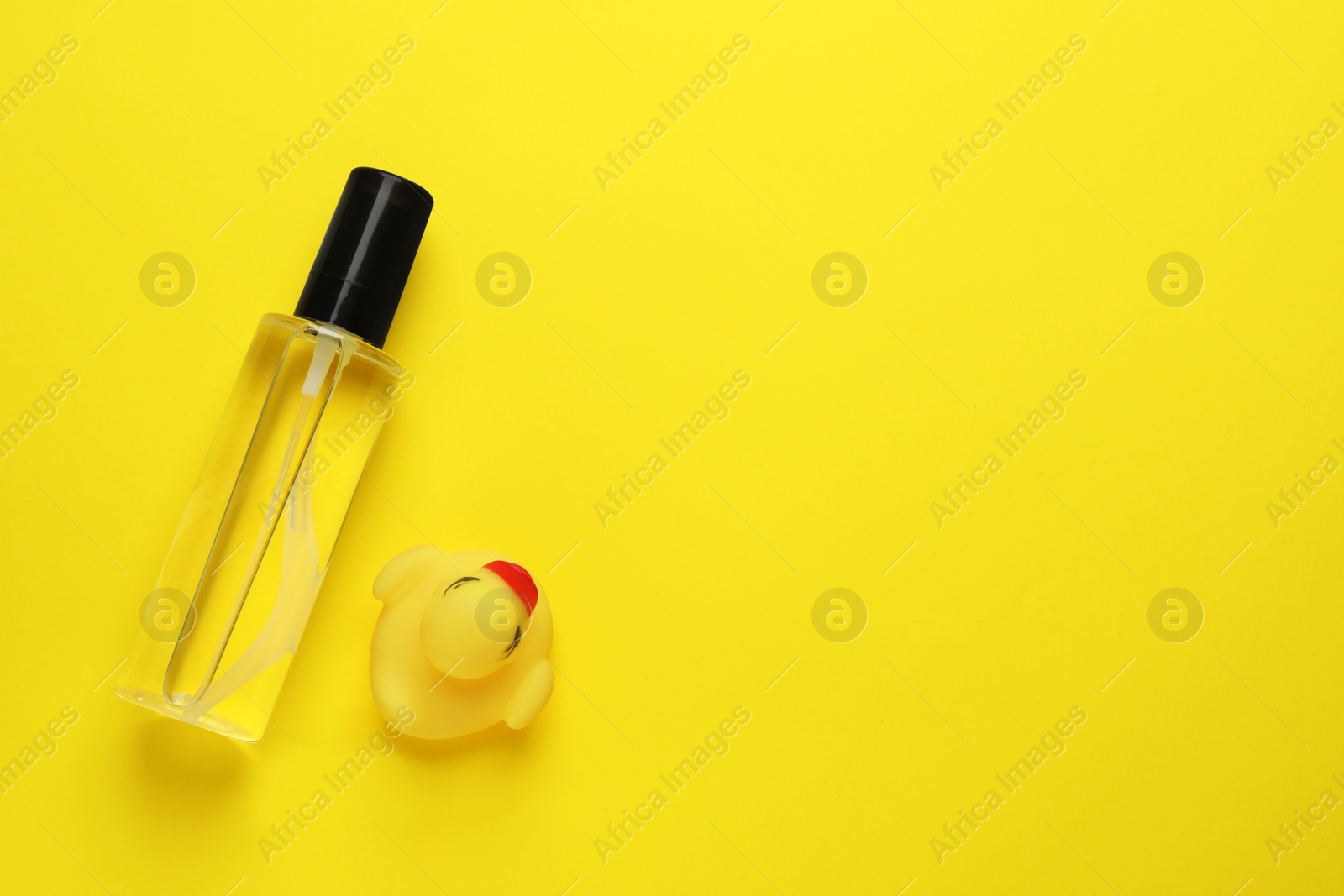 Photo of Bottle of baby oil and toy duck on yellow background, flat lay. Space for text