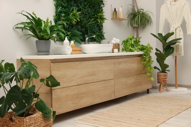 Green artificial plants, vanity and different personal care products in bathroom