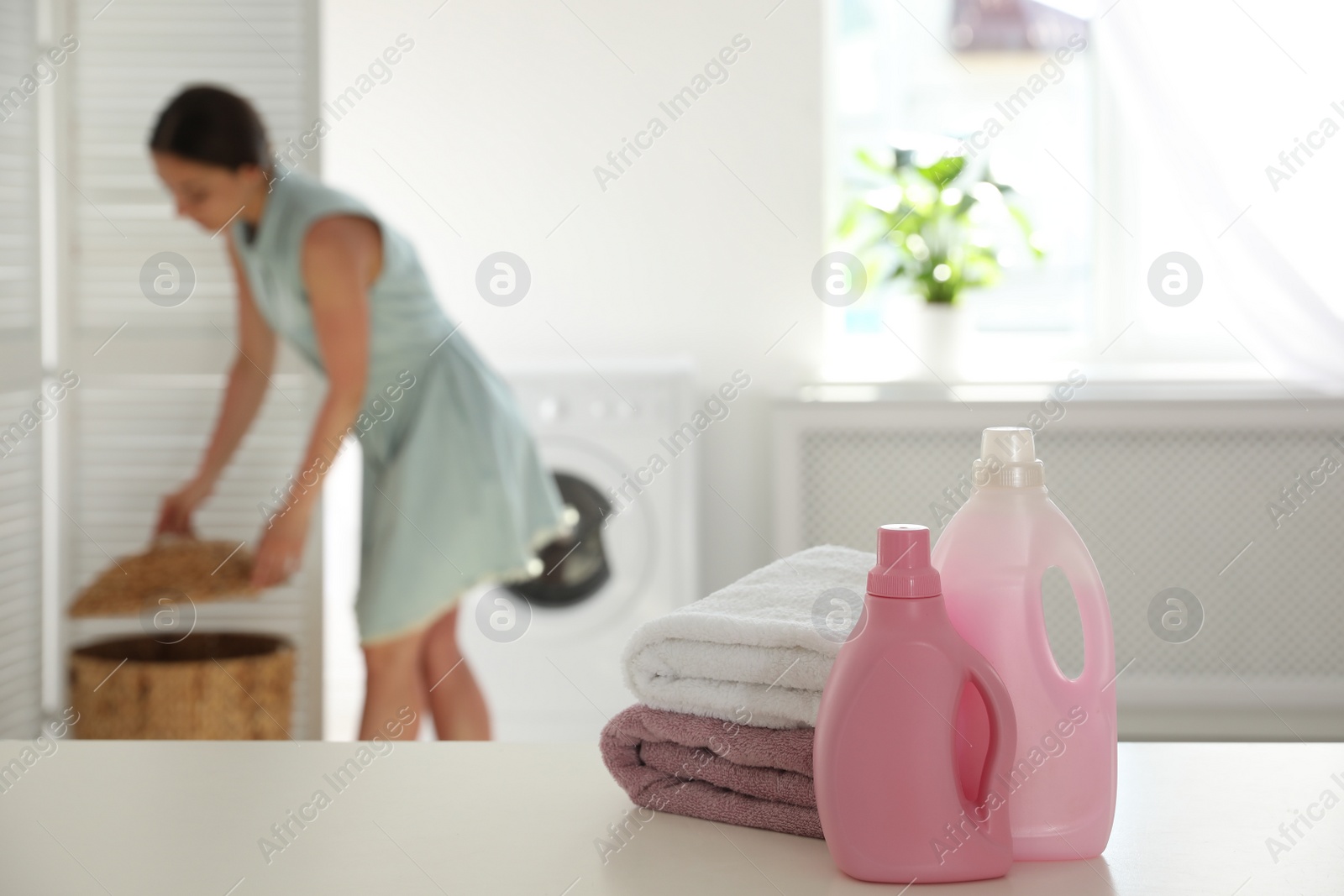 Photo of Stack of clean towels, detergents and blurred woman on background. Space for text