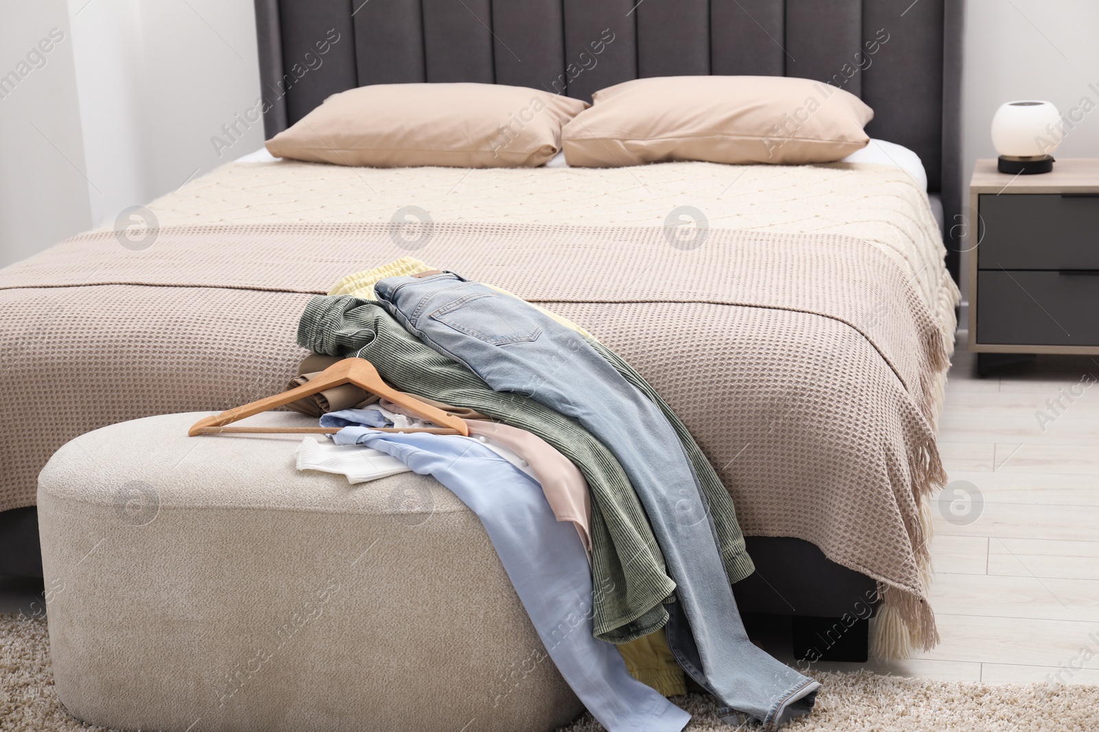 Photo of Many different clothes on ottoman in bedroom