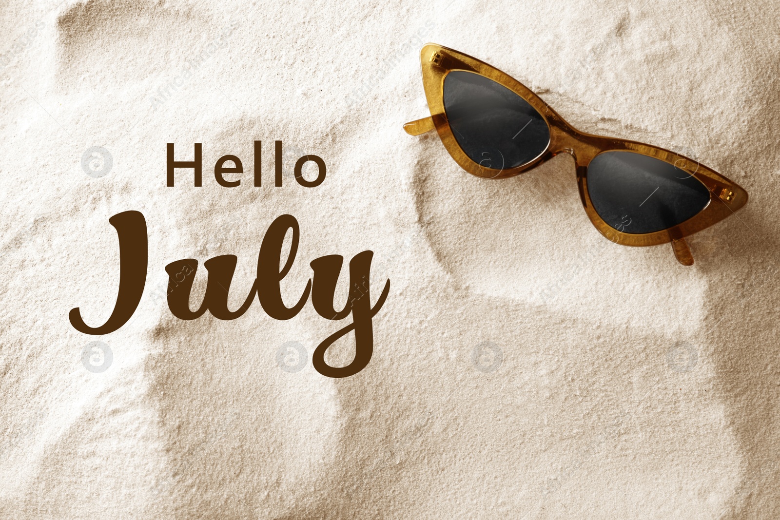 Image of Hello July. Stylish sunglasses on sand, top view