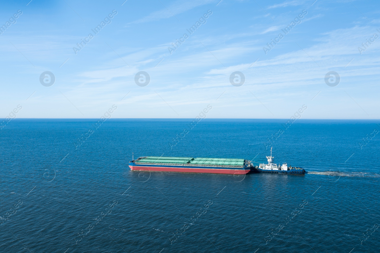 Image of Tugboat pulling barge with cargo by water, aerial view